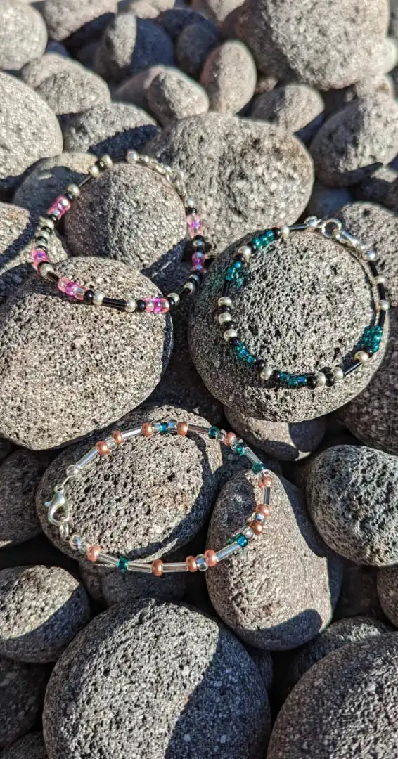 Three of our beautiful Morse code bracelets placed across some fire pit rocks.